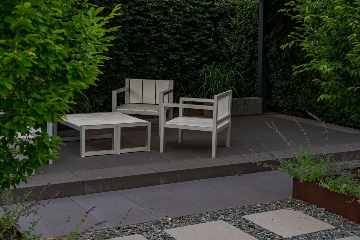 A peaceful outdoor patio with simple wooden furniture surrounded by a vibrant garden, ideal for branding inspiration.